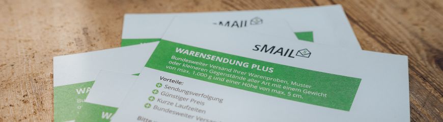 Postkarten von sMAIL wo die Vorteile der Warensendung Plus draufstehen, liegen auf dem Tisch