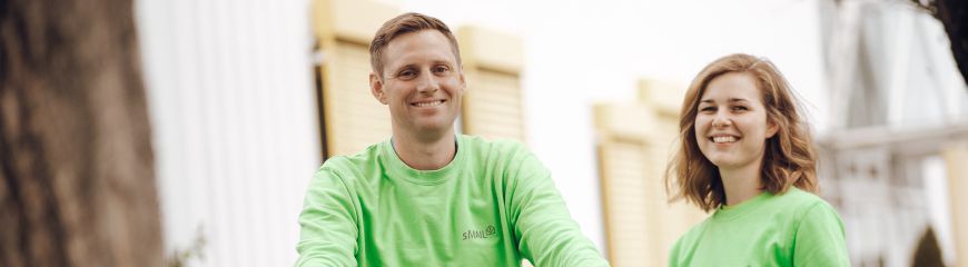 Eine Frau und ein Mann. Beide lächeln und tragen einen grünen sMAIL Pullover