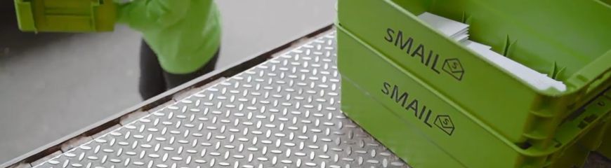 Grüne Kisten mit Briefen darin werden von einer Person im sMAIL Pullover auf die Rampe getan