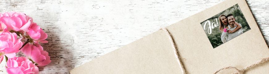 eine Briefmarke klebt auf einem Brief und dieser liegt mit einer pinken Blume auf dem Tisch