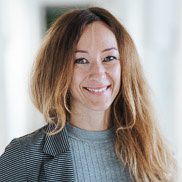 Eine Frau mit langen Haaren die ein hellgraues Oberteil und ein dunkelgrauen Blazer an hat