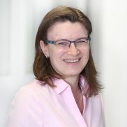 Eine Frau mit mittellangen Haaren und einer Brille. Sie hat eine rosane Bluse an